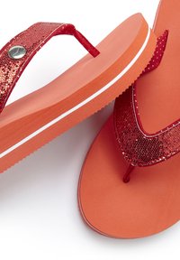 Red flip-flops with textured glittery straps, an orange rubber sole, and white accent lining. Smooth surface and toe post design.