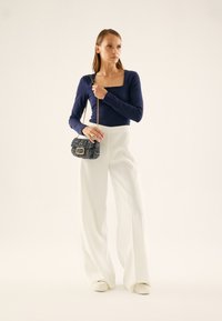 Long-sleeve navy top with square neckline, paired with high-waisted white wide-leg pants. Model holds a small textured black handbag.