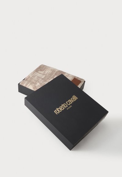 Μαύρο κουτί με χρυσό κείμενο "roberto cavalli HOME" περιέχει διπλωμένο μπεζ υφασμάτινο ύφασμα με σχέδια μέσα.