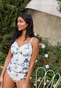 Blumiges Zweiteiler-Bikini mit verstellbaren Trägern; hat eine weiße Grundfarbe mit blauen und grünen botanischen Mustern und einem leicht strukturierten Stoff.
