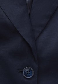 Blazer bleu marine en tissu texturé, avec des revers notch et une fermeture à boutons ronds à quatre trous.