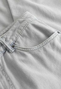 Gros plan sur un tissu en denim bleu clair montrant la poche avant, la passants de ceinture et le détail rivet en métal sur un jean.