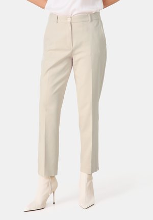 Beige maßgeschneiderte Hosen mit schmaler Passform, weicher Textur und Falten an der Vorderseite, kombiniert mit eleganten weißen spitzen Stiefeletten.