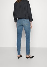 Slim-fit džíny ve středně modré barvě, s dvěma zadními kapsami a středním pasem, doplněné volnou černou košilí a černými podpatky.