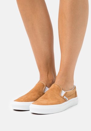 Mörkbeige slip-on skor i mocka med vita gummisulor; har elastiska detaljer vid sidorna och en texturerad ovansida.