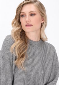 Pulover gri din tricot cu guler înalt și umeri căzuți. Material texturat cu nervuri vizibile și o siluetă relaxată.