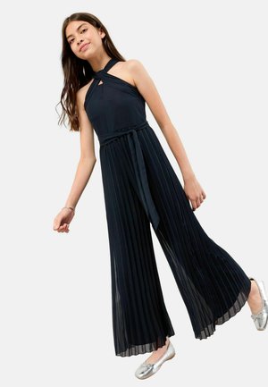 Mørkeblå plisseret jumpsuit med halterneck, der har en talje-bånd og let brede ben. Sølvfarvede ballet flade sko supplerer outfittet.