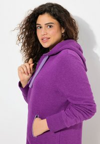 Felpa viola realizzata in tessuto morbido, con cappuccio regolabile, tasche laterali e polsini a costine. Il design include dettagli a contrasto.
