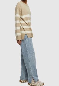 Pull en tricot à rayures beiges avec un col rond, associé à un jean bleu clair à jambes larges avec des fentes sur le côté et des baskets crème.