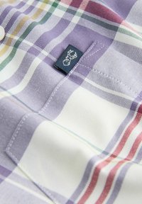 Kariertes kurzärmliges Hemd mit lila, weißen und roten Streifen; verfügt über ein kleines Logo-Tag mit Geweih-Design, aus weichem Baumwollstoff hergestellt.