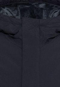 Marynarka w kolorze granatowym, wyróżniająca się gładkim, teksturowanym wykończeniem oraz miękkim, ciemnoszarym futerkiem w środku. Posiada wysoki kołnierz oraz ukryty zamek. 