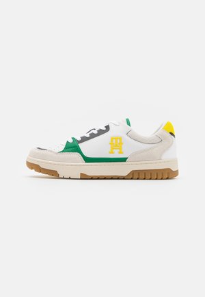 Hvid lavtop-sneakers med grønne og gule accenter, beige ruskind detaljer og en tan gummisål, der viser en sideprofil.