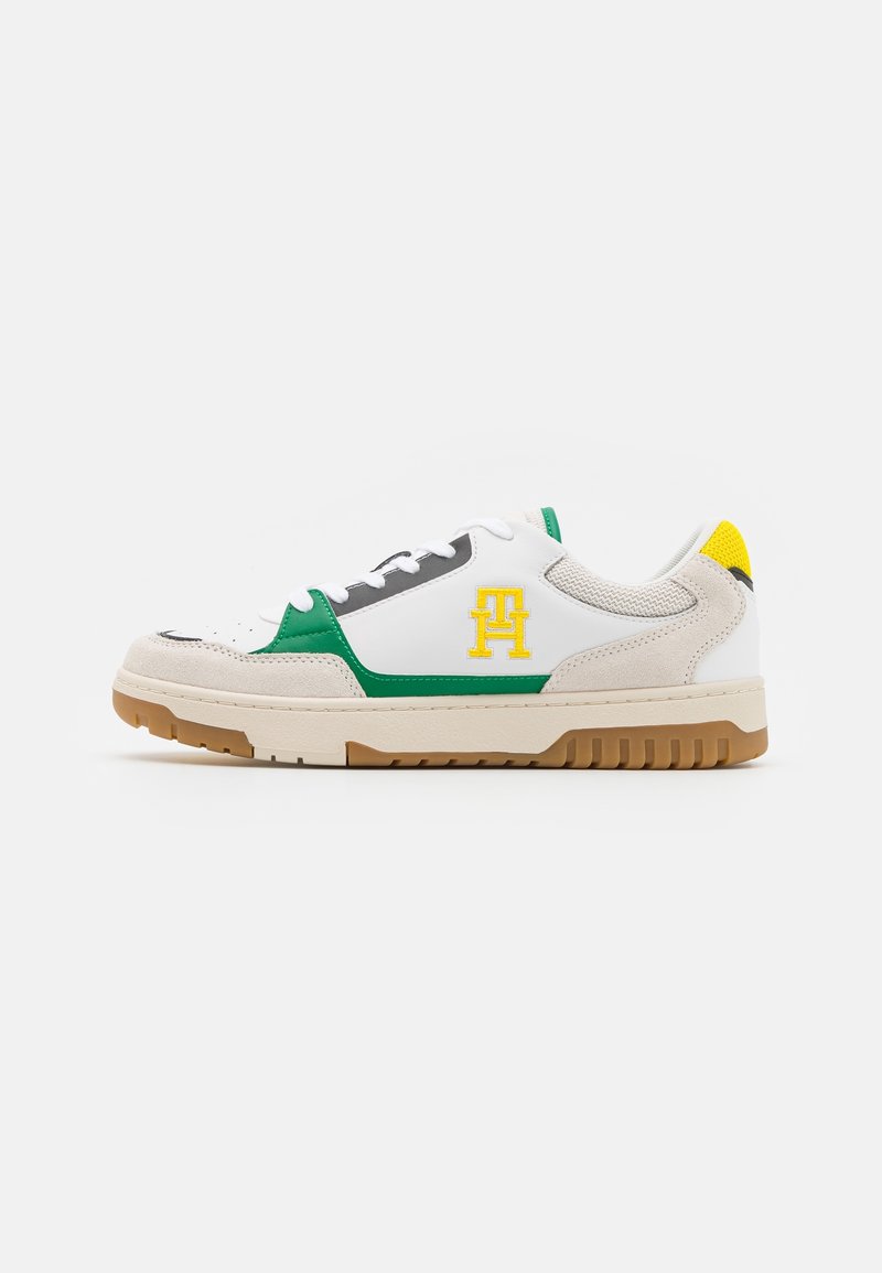 Baskets basses blanches avec des accents verts et jaunes, des détails en daim beige et une semelle en caoutchouc couleur fauve, vue de profil.