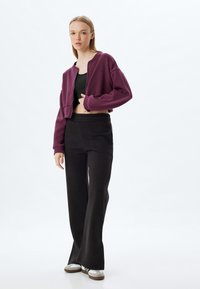 Sudadera morada recortada, top negro y pantalones acampanados negros; textura suave, diseño sin costuras; combinada con zapatillas blancas y grises.