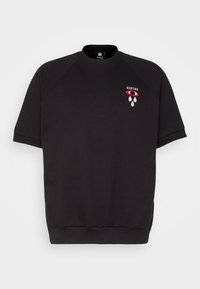 Svart sweatshirt med korta raglanärmar, rundad halsringning och en liten broderad grafik i rött och vitt som föreställer ett öga och droppar.