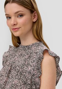 Lichtgewicht mouwloze blouse met een gerimpelde halslijn, met een roze en zwart gevlekt patroon. Gladde stof met een subtiele textuur.