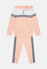 Peach tracksuit featuring a zip-up hoodie with white panel and gathered sleeves, paired with matching leggings with navy "GUESS LOVE" side stripes.