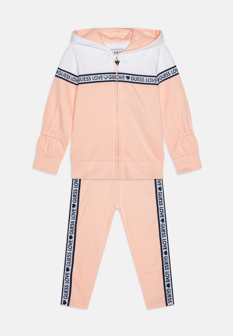 Peach tracksuit featuring a zip-up hoodie with white panel and gathered sleeves, paired with matching leggings with navy "GUESS LOVE" side stripes.