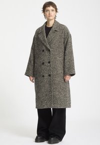 Dobbeltbrystet frakke i et sort-hvidt houndstooth mønster, med store knapper, brede revers og en afslappet pasform. Tekstureret uldstof.