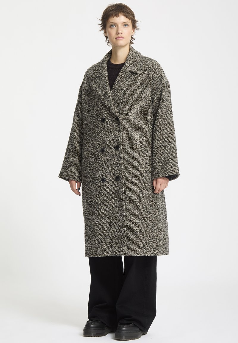 Dobbeltbrystet frakke i et sort-hvidt houndstooth mønster, med store knapper, brede revers og en afslappet pasform. Tekstureret uldstof.