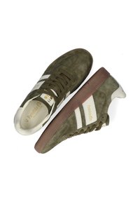 Groene suède sneakers met witte strepen, ronde neus, bruine rubberen zool en gouden branding aan de binnenkant. Heeft een vetersluiting en een zachte textuur.