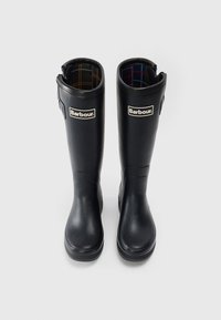 Zwarte rubberen kniehoge laarzen met een gladde textuur, een geruite voering en een zichtbaar Barbour-logo op de voorkant.