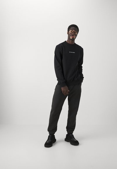 Black sweatshirt with a crew neck and white text on the chest, paired with dark gray tapered joggers and black chunky-soled boots.