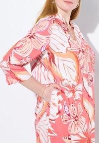 Blommönstrad klänning med rosa och orange nyanser, avslappnad passform, trekvartsärmar och sidfickor. Släta tyger med en livlig design.