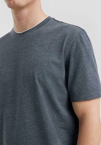 T-shirt en gris foncé à col rond et manches courtes, fabriqué à partir d'un tissu doux et texturé. Il présente un design simple et épuré sans logos visibles.