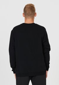 Svart sweatshirt med rund hals i mjukt material. Långa ärmar med ribbade muddar och ribbad midja. Enkelt bakifrån.