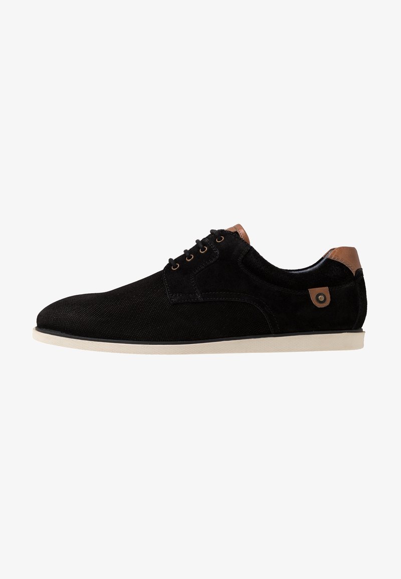 Chaussure noire en daim à lacets avec un bout arrondi, accent de talon beige contrastant, œillets en métal et semelle en caoutchouc blanche.