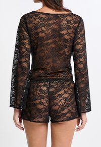 Zwarte kanten set met een langwerpige top en shorts, die fraaie bloemmotieven en een transparante textuur toont.