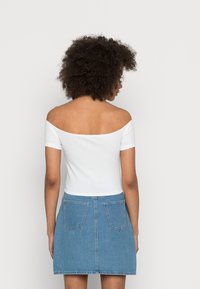 Top corto acanalado blanco con hombros al descubierto, combinado con una falda A-line de mezclilla azul claro que presenta dos bolsillos traseros y un ajuste casual.