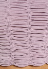 Ruched pink fabric dengan lipatan horizontal, tekstur halus, dan hem scallop. Detail menekankan desain yang elastis dan membentuk tubuh.