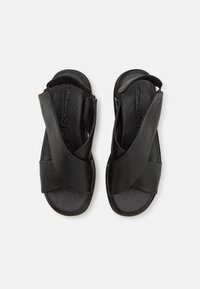 Sandales en cuir noir dotées de brides croisées à l'avant, d'une semelle intérieure rembourrée et d'une bride de talon réglable pour un maintien sûr. Texture lisse.