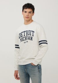 Jasnoszary sweter z napisem "DETROIT MICHIGAN EST 82" w granatowym kolorze, poziome granatowe paski na rękawach, okrągły dekolt i ściągacz w talii.