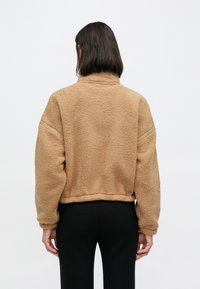 Hnedá mikina z flísu s vysokým golierom, spustenými ramenami a skrátenou dĺžkou. Mäkká textúra s jednoduchým dizajnom, vhodná na bežné nosenie.