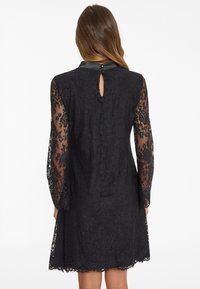 Black lace dress featuring a sheer long-sleeve design, a small keyhole at the back, and a leather-like collar with button accents.