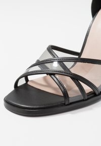 Svarta klacksandaler med genomskinliga remmar, med fyrkantig tå och slät läderliknande yta. Minimalistisk design med korsremmar.