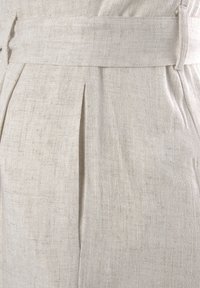 Crème-kleurige linnen stof met zichtbare textuur, voorzien van een voorplooien en een geweven riemdetail voor sluiting. Elegante en op maat gemaakte design.