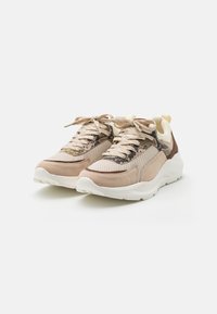 Baskets beige et marron avec semelles blanches épaisses, panneaux en mesh et suède, lacets noués en nœuds, présentées sur un fond blanc.