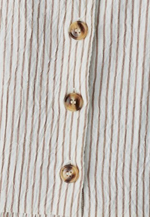 White and brown striped fabric with a wrinkled texture, featuring four round, shiny buttons with a two-hole design.