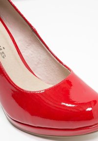 Escarpin pour femme en cuir verni rouge avec bout arrondi et semelle intérieure beige rembourrée sur fond blanc.