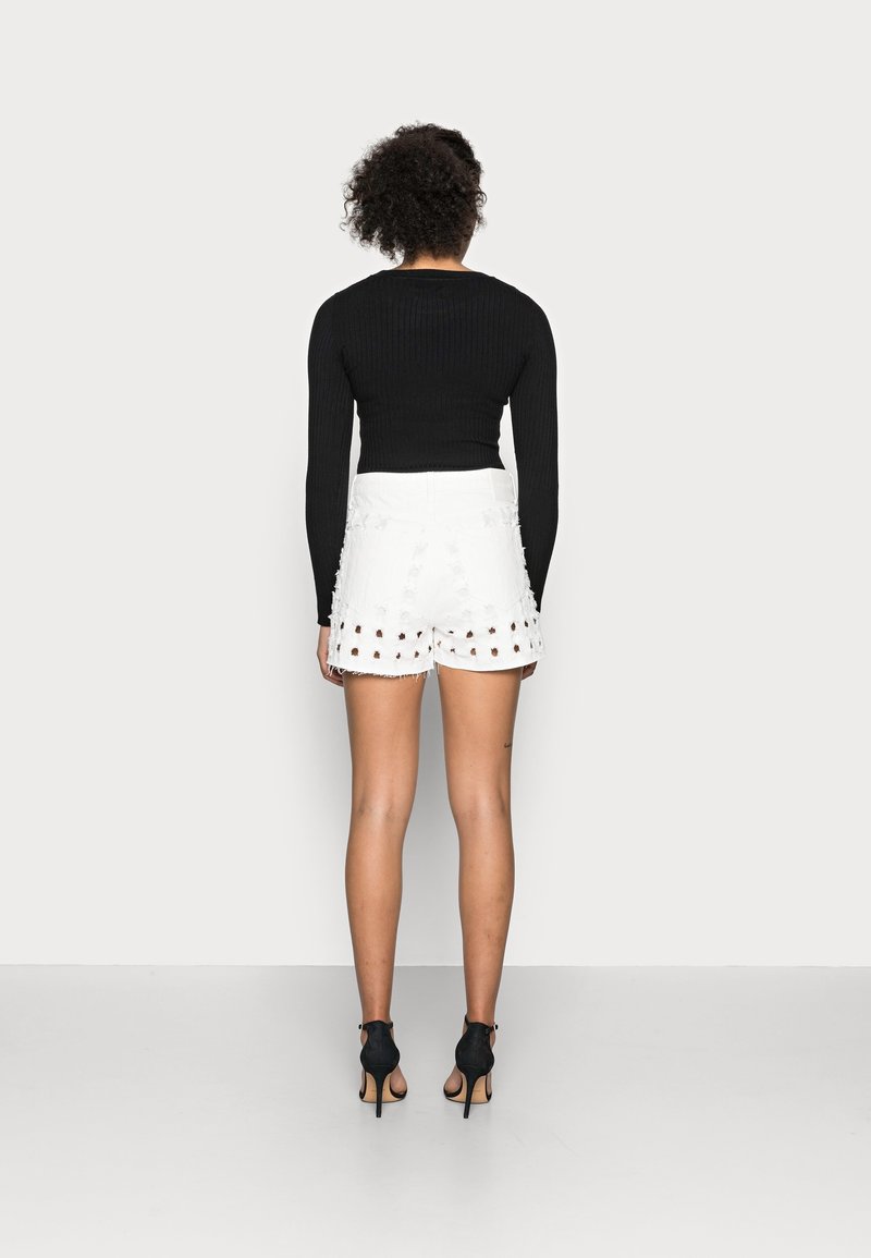 Top negro de manga larga con canalé combinado con shorts blancos de dobladillo deshilachado con cortes y detalles, llevados con zapatos de tacón negros.