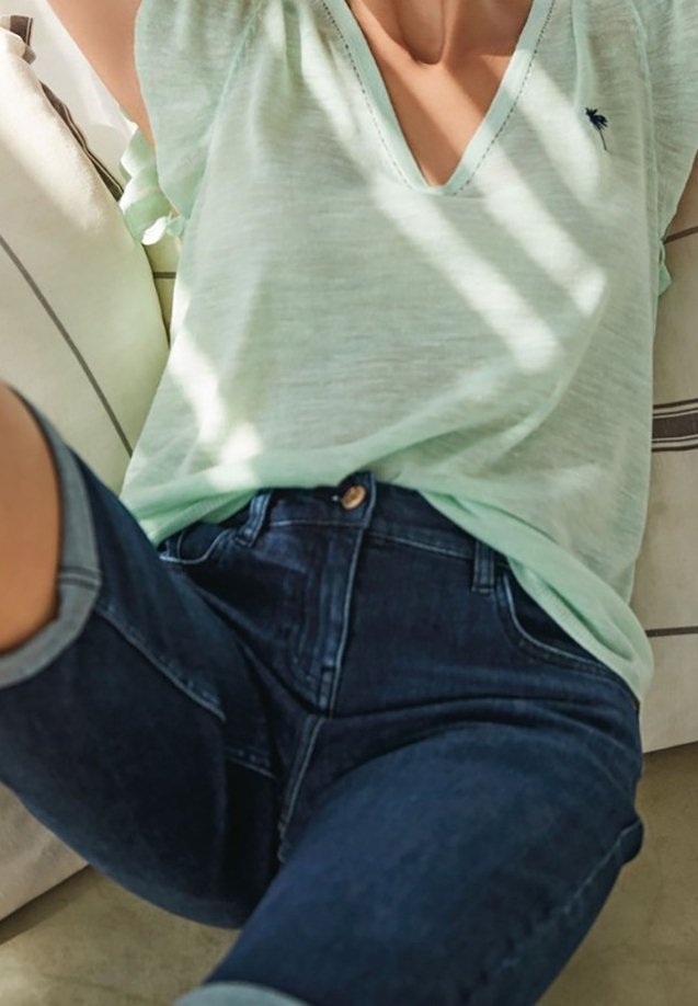 Jasnozielony top z dekoltem w serek i krótkimi rękawami, zestawiony z ciemnoniebieskimi dżinsami z wysokim stanem, zapinanymi na guziki i podwiniętymi mankietami.