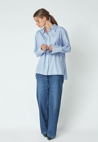 Light blue striped button-up shirt with long sleeves and a chest pocket, paired with wide-leg dark denim jeans. Smooth texture, casual fit.