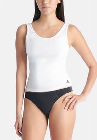 Hvit ribbestrikket tanktopp med rund hals, med en liten svart Adidas-logo nederst til venstre. Kombinert med svarte bikinibukser.