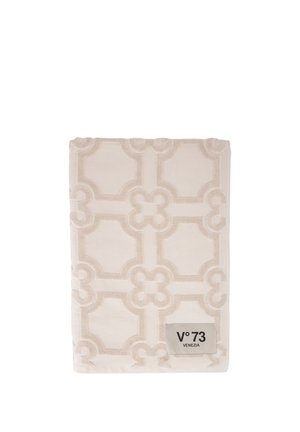 Asciugamano beige piegato con motivo geometrico in rilievo e etichetta "V°73 VENEZIA" cucita nell'angolo.