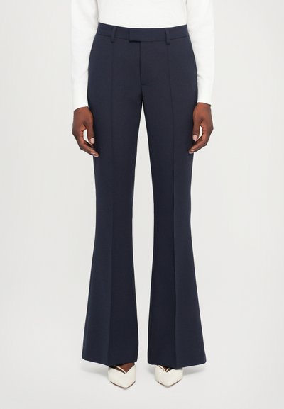 Pantalones de campana en color marino, confeccionados con una tela suave, que presentan un frente plano, trabillas para cinturón y un ajuste entallado, combinados con tacones blancos de punta.