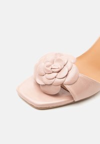 Κοντινή λήψη ενός ανοιχτόροζ σανδαλιού με τετράγωνη μύτη, που διαθέτει μια μεγάλη διακοσμητική δερμάτινη ανθοδέσμη στο λουράκι.